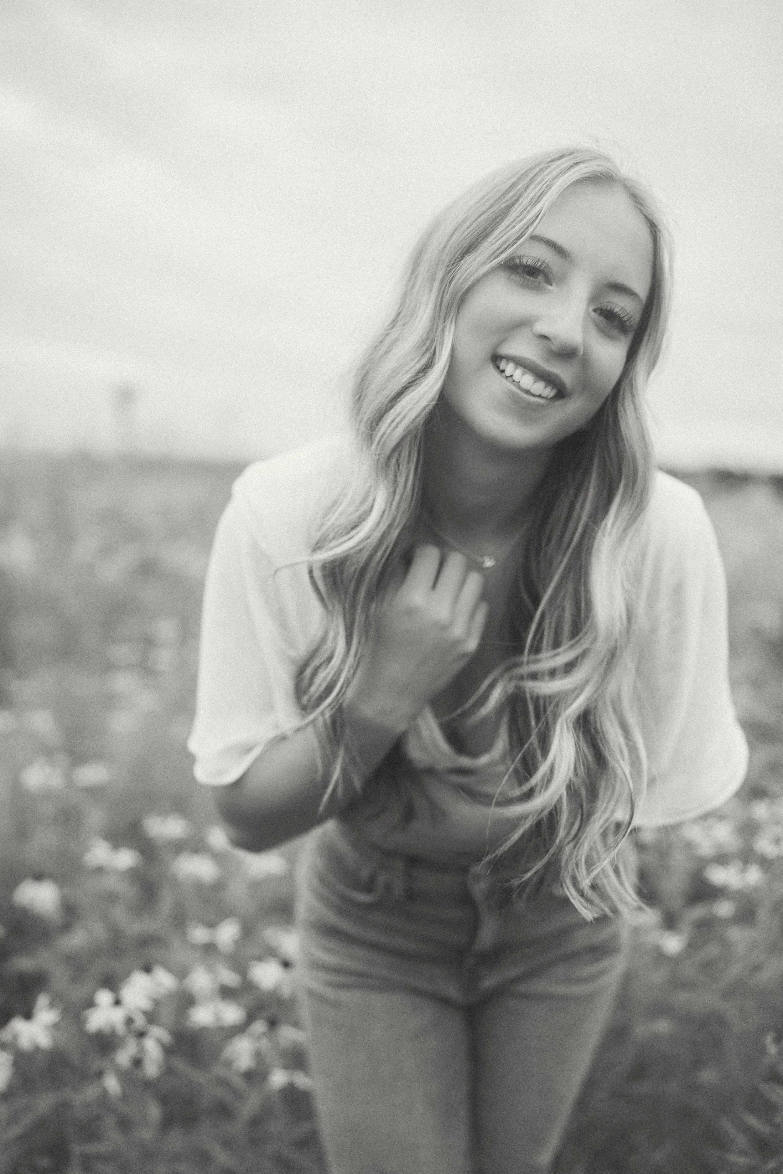 A young woman smiling outdoors in a field of flowers, black and white.