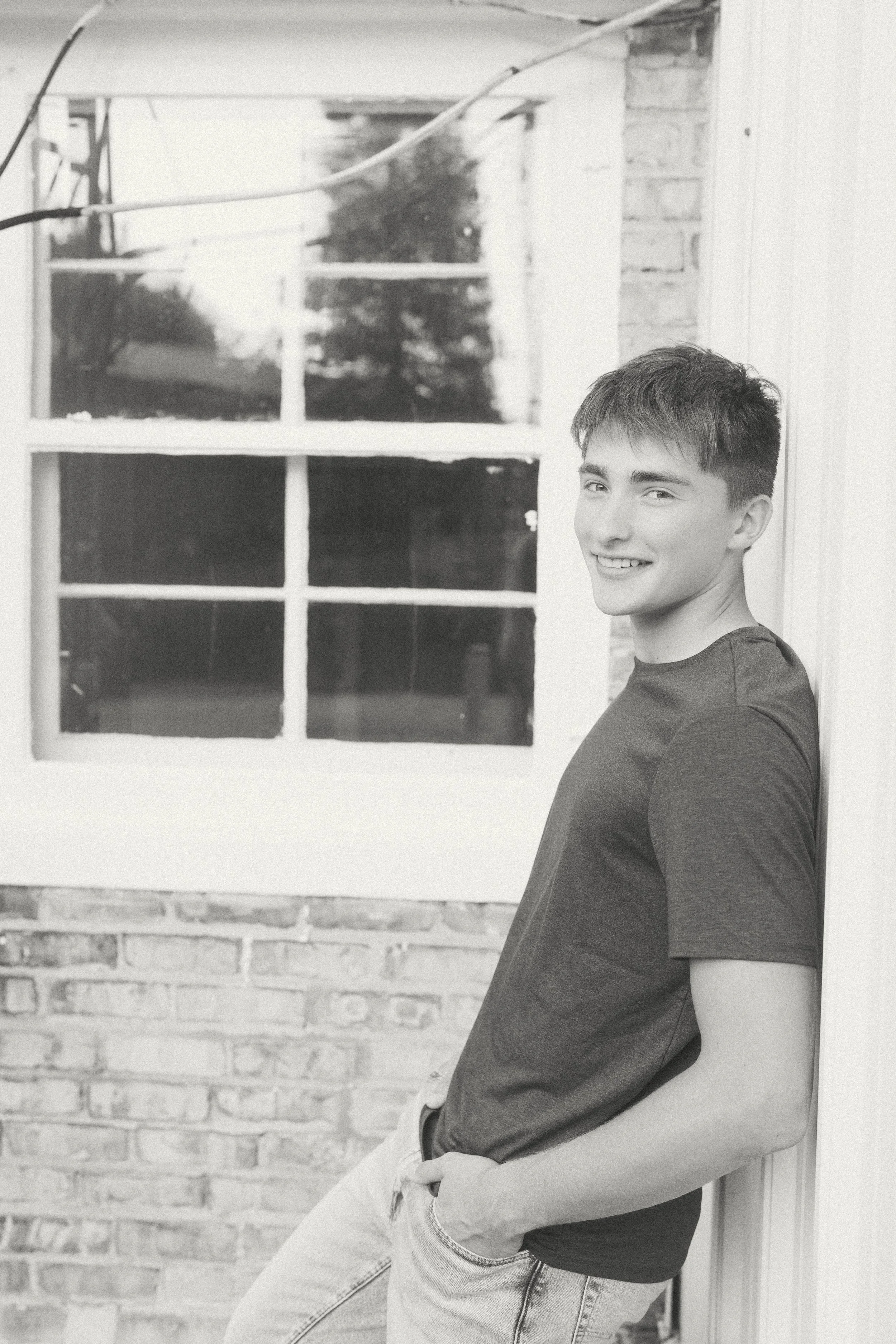 A young man leaning against a wall outside, smiling at the camera.