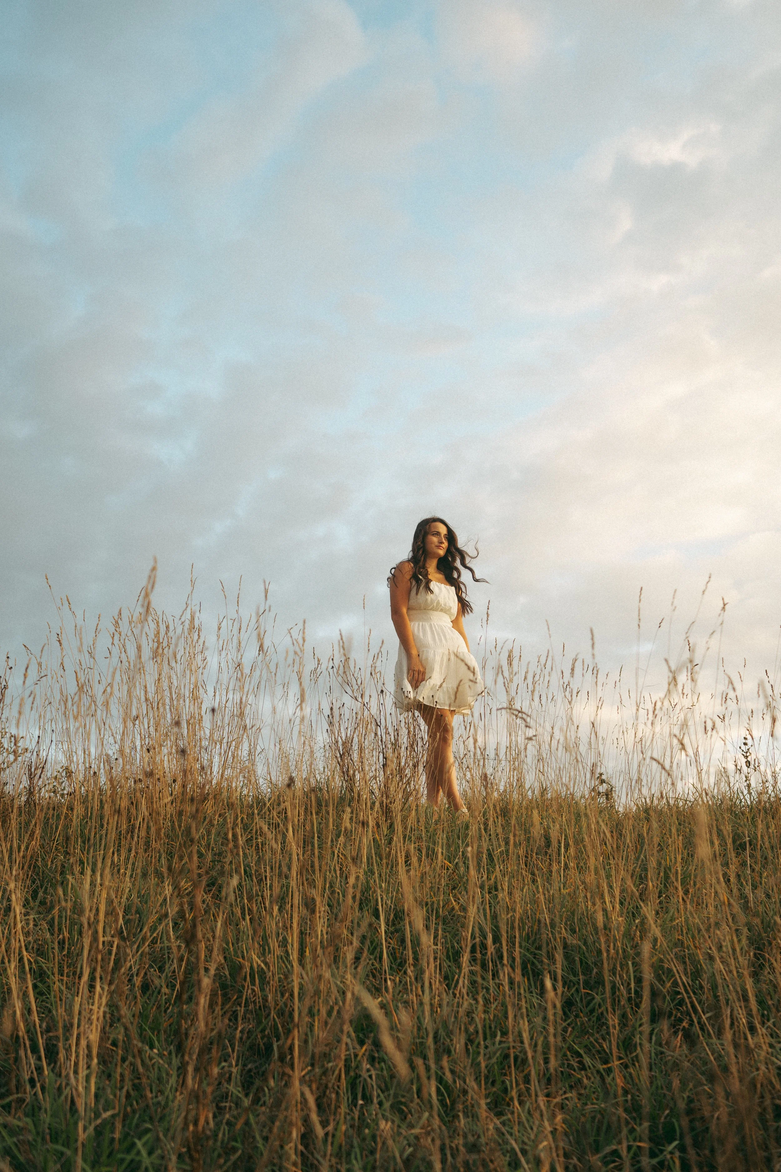 A woman in a white dress standing in a grassy field at sunset.