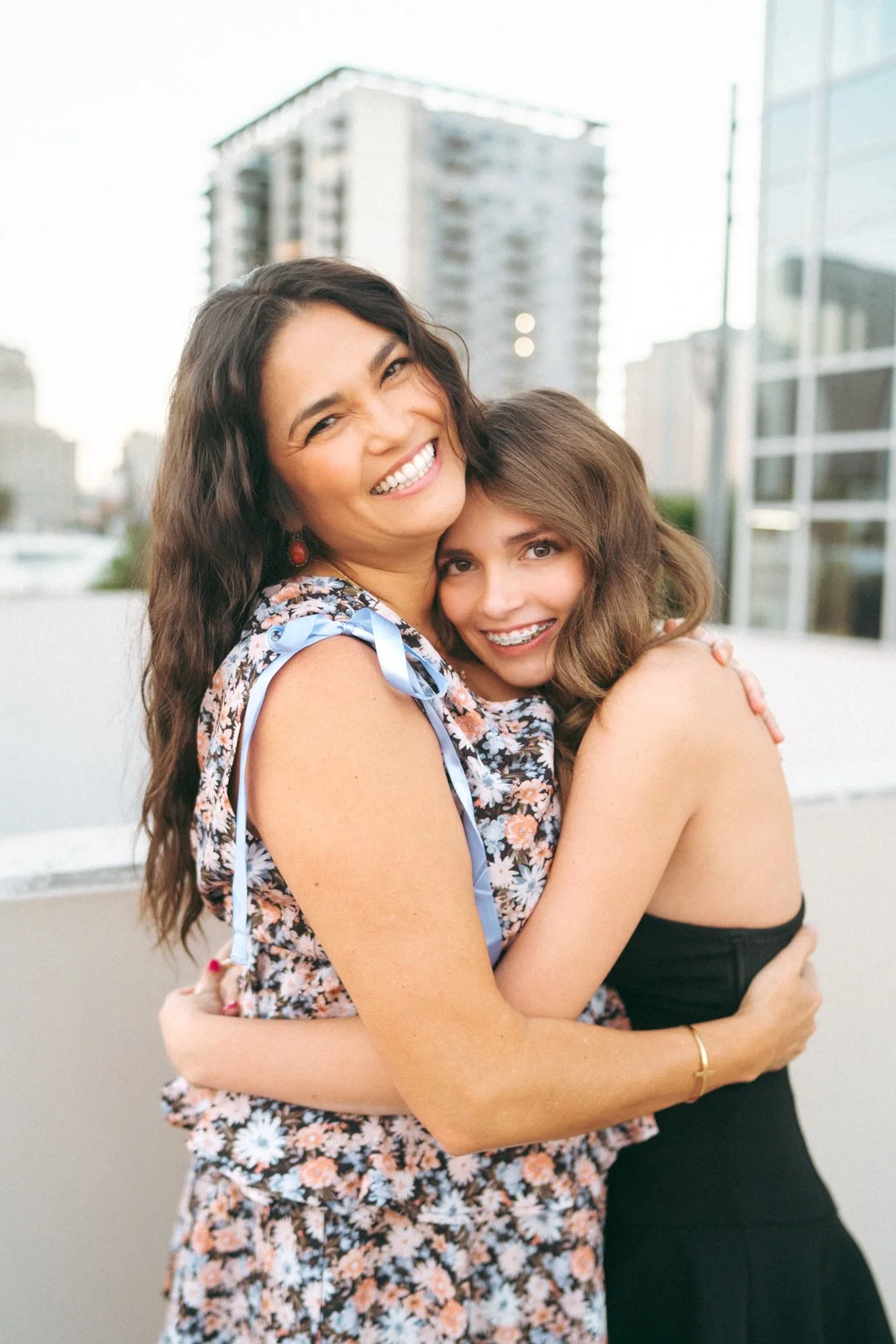 Two women hugging and smiling outdoors in an urban setting.