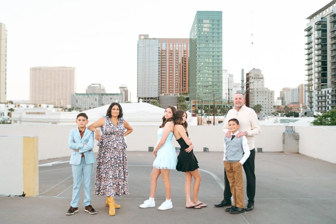 A diverse family standing on a rooftop with a city skyline in the background, including five children and one adult man.