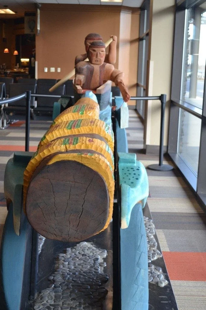 The magnificent sculpture depicts two Lummi Coast Salish fishermen in a shovel-nosed canoe, pursuing a salmon with a gaff hook. At the other end of the story pole a serpent is after the same salmon, its mouth reaching for the fish. The Coast Salish fishermen wear spiritual paint on their faces, signifying the spiritual healing of the salmon.