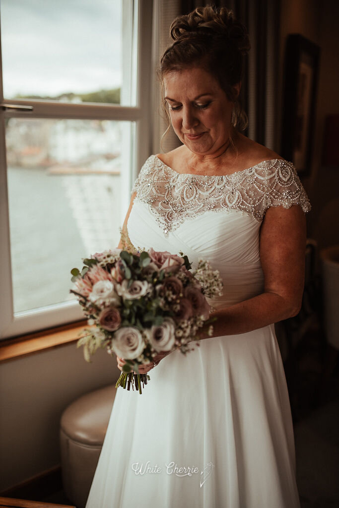 Scottish bride standing by window at Orrocco Pier holding bridal bouquet. 
