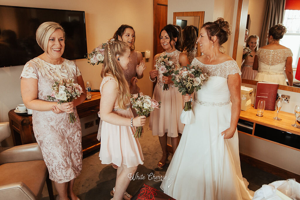 Scottish bride laughing with bridal party holding beautiful wedding flowers. 