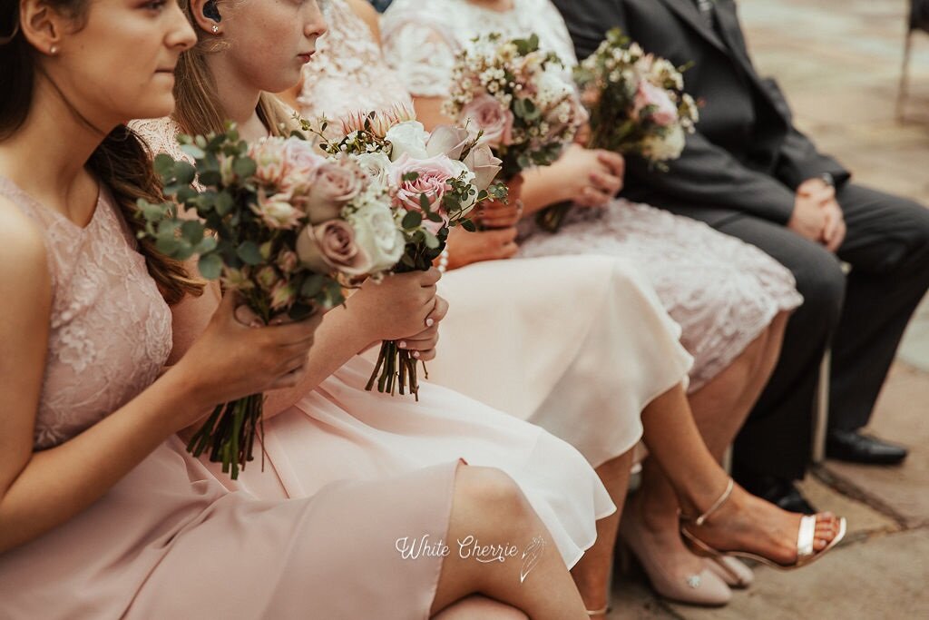 Bridesmaids in dusky pink and cream dresses holding wedding flowers by Stunning Flowers.