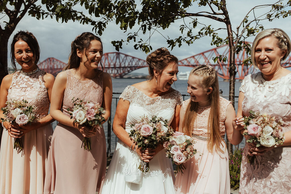 Scottish Bridal party standing in front of Forth Rail Bridge holding wedding flowers.