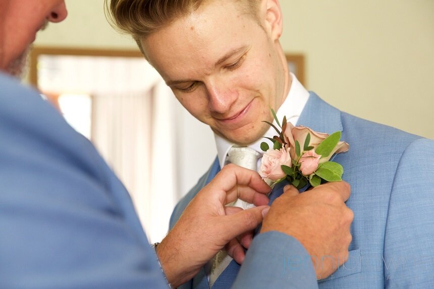 Groomsman pinning buttonhole to grooms lapel. 