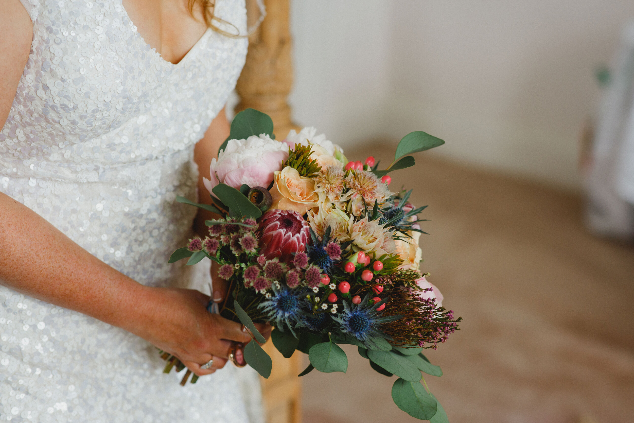 Bride holding beautiful bridal bouquet of berries, protean eryngium, peonies and mixed roses at Strathallan Castle