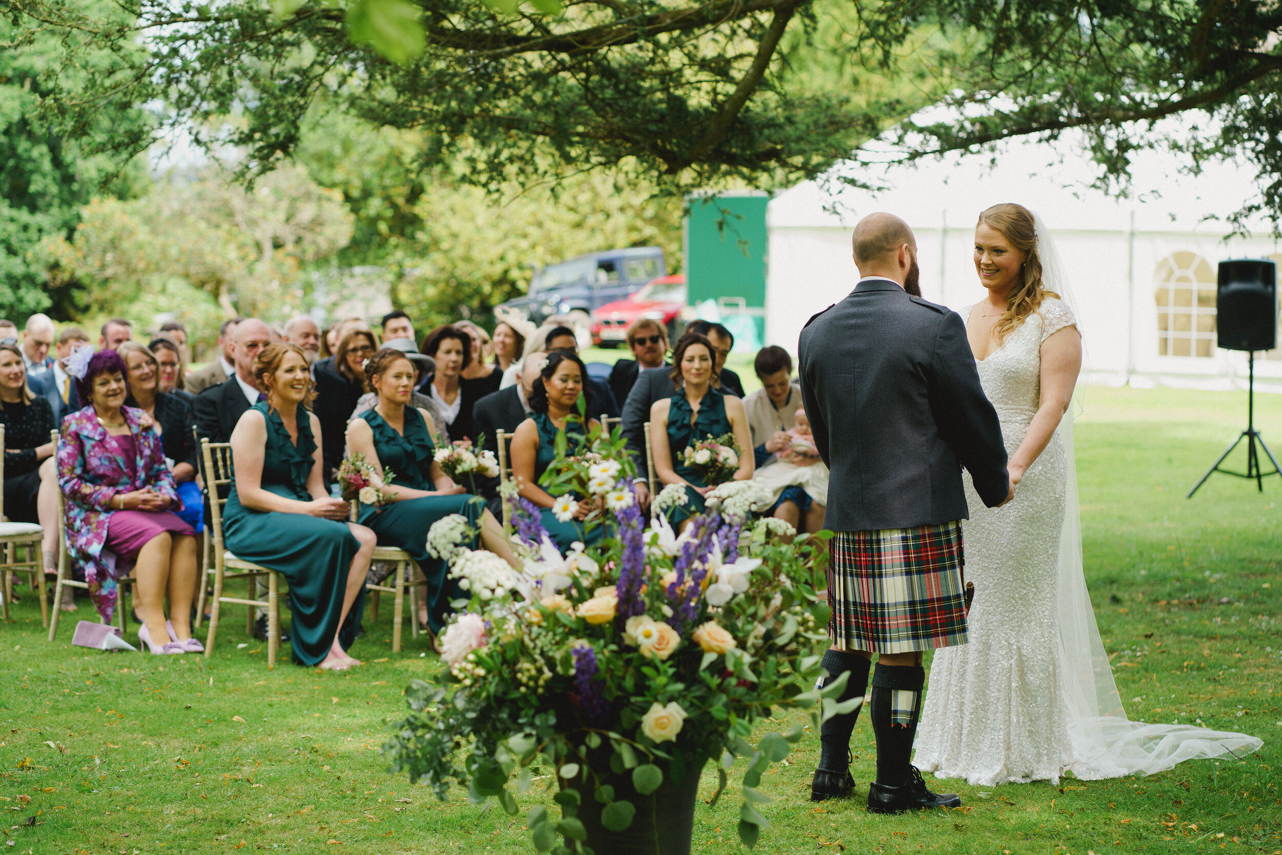 Bride and Groom getting married outside at Strathallan Castle, surrounded by guests and beautiful wedding flowers. 