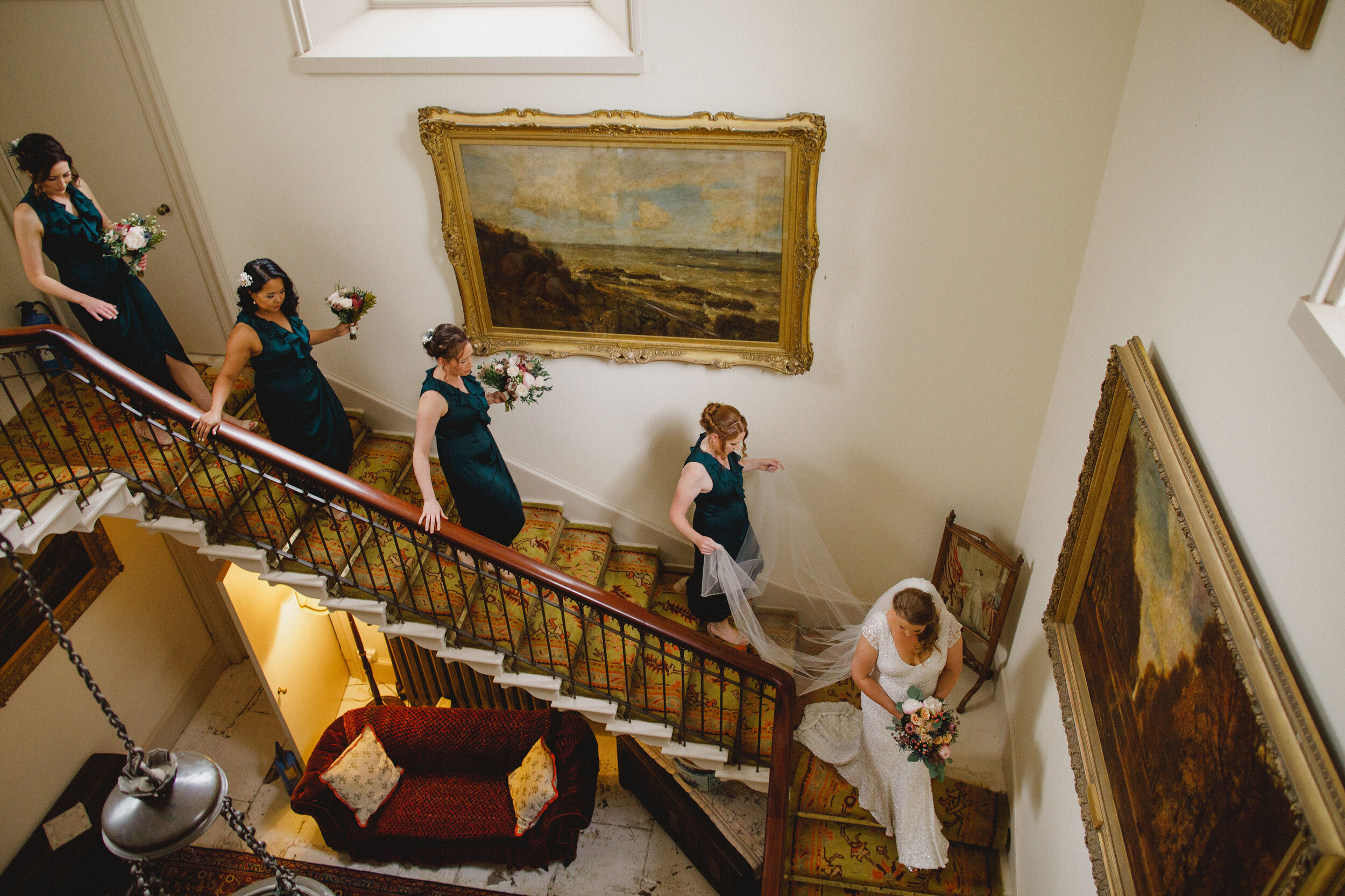 Bridesmaids wearing navy dresses walking down stair case behind bride holding on to wedding flowers at Strathallan Castle, Perthshire.