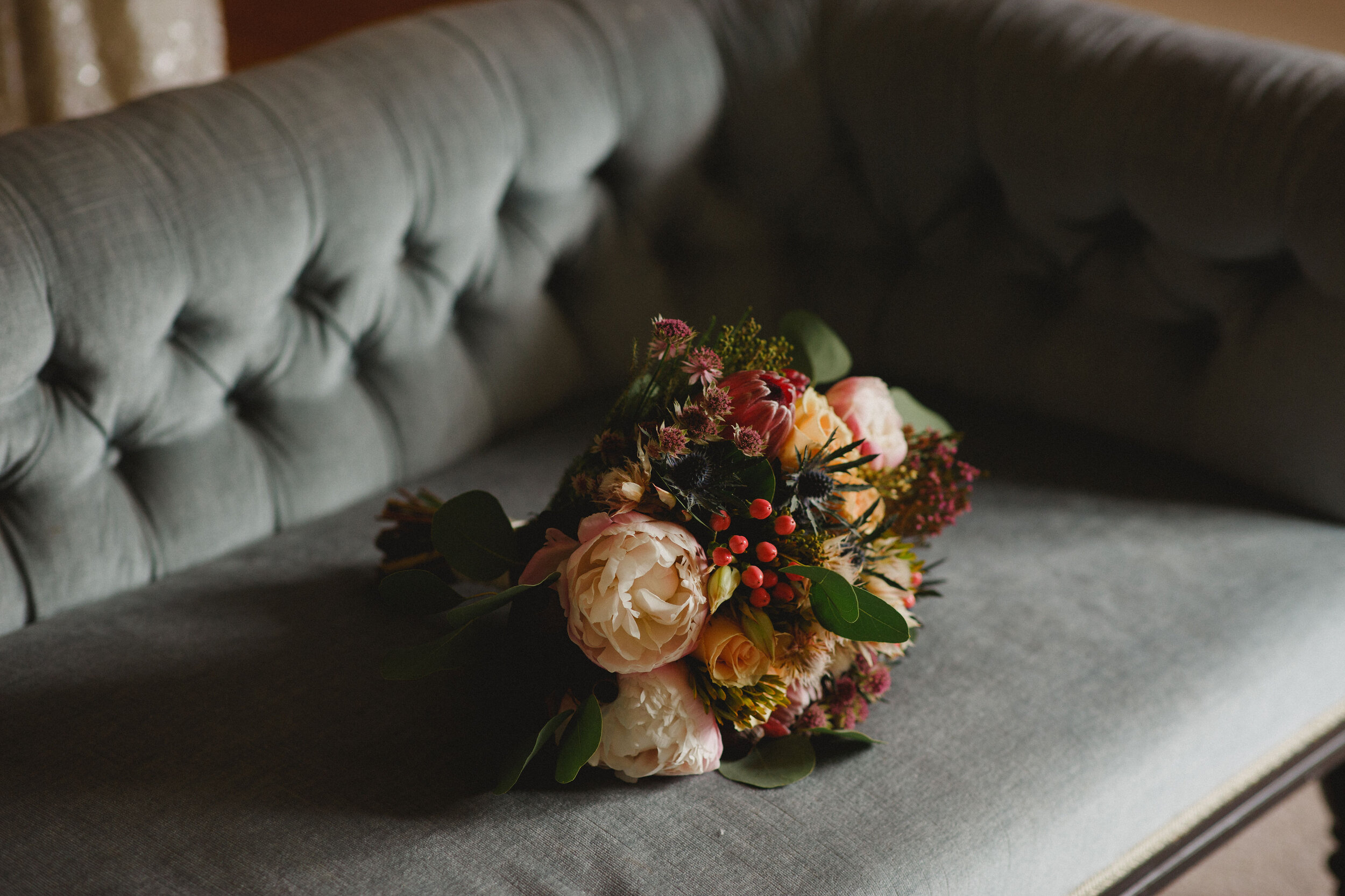 Peonie, Eucalyptus and berry wedding bouquet lying on grey sofa at Strathallan Castle, Perthshire.