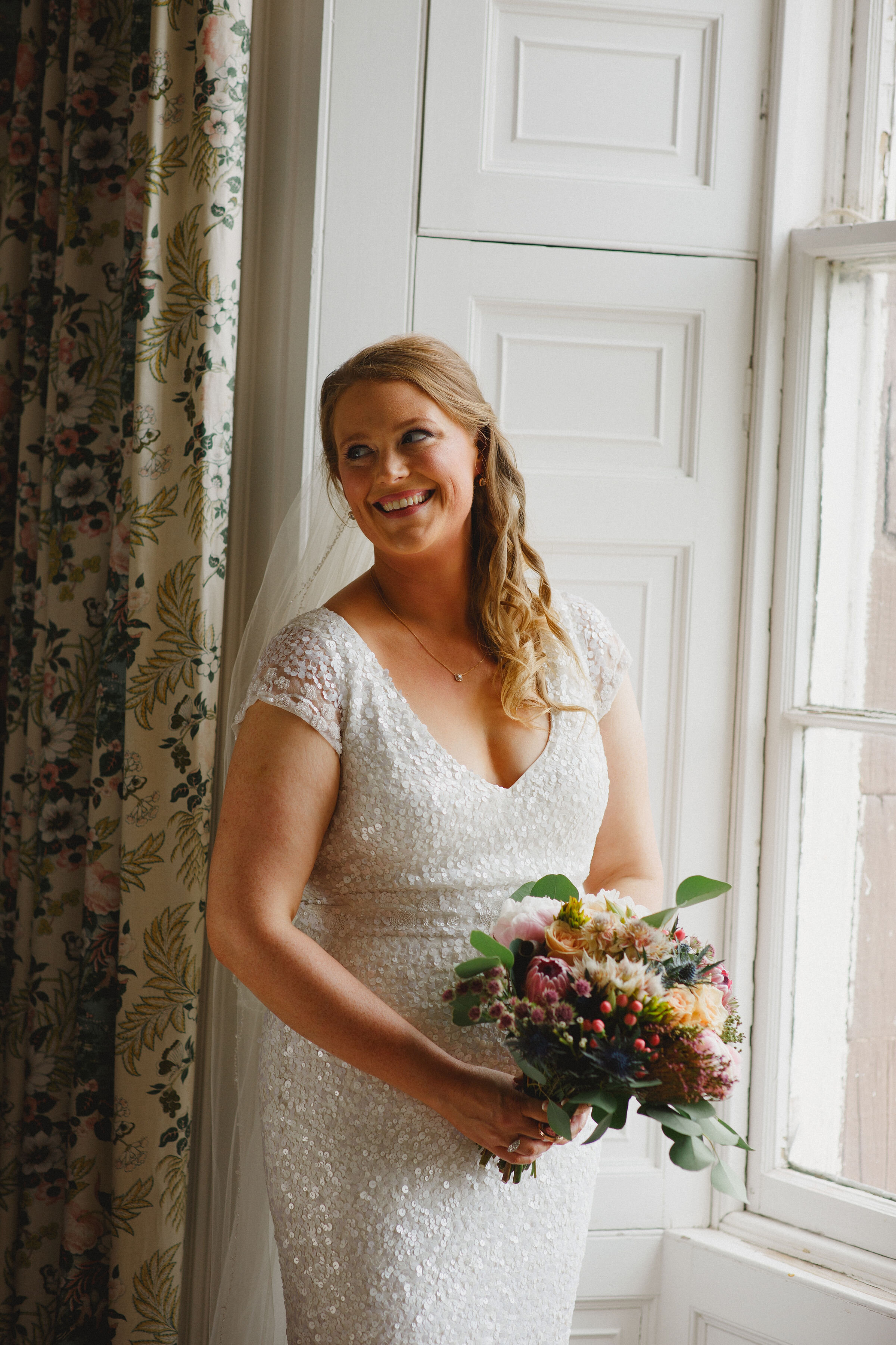 Bride standing next to window holding her bouquet at Strathallan Castle, Perthshire