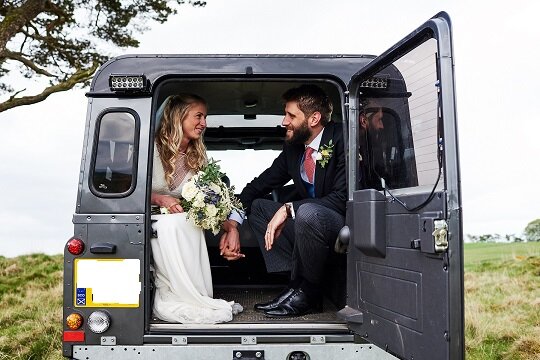 Bride and groom sitting in Landrover Defender, bride holding wedding bouquet.