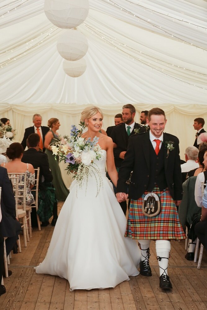 Bride and Groom walking up the aisle after getting married, bride holding a loose tied bouquet of Scottish flowers. 