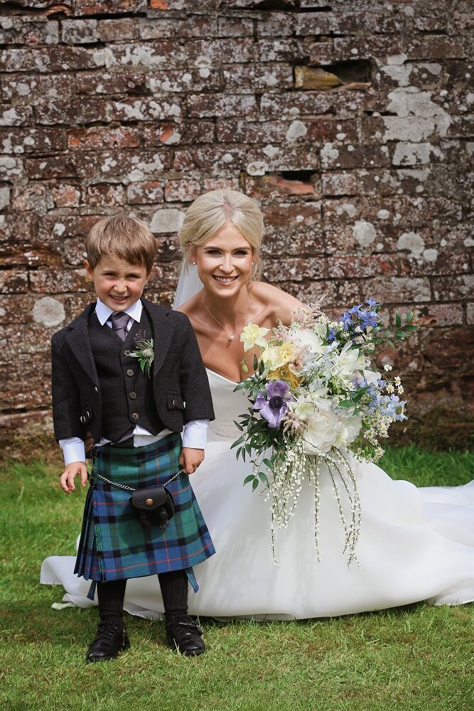 Bride crouching next to page boy holding her cream and pastel wedding bouquet at Perthshire wedding 