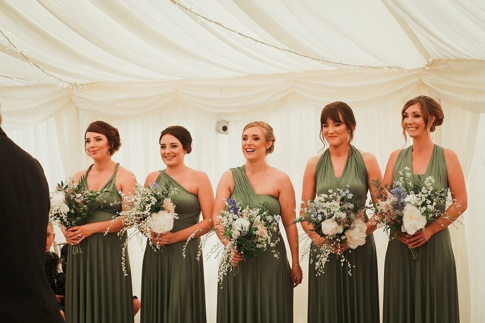 Bridesmaids wearing green dresses holding bouquets of peony, delphinium and daisies