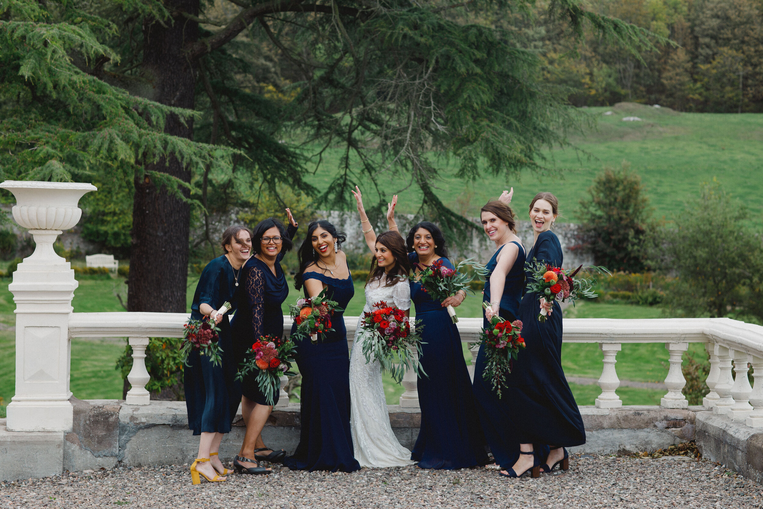 Braidsmaids in navy gowns standing with brides showing off their bridal bouquets at Carphin house. 