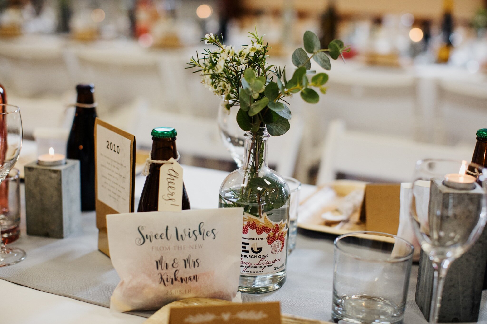 Wedding tablescape featuring gin bottles with posies of wax flower and Eucalyptus