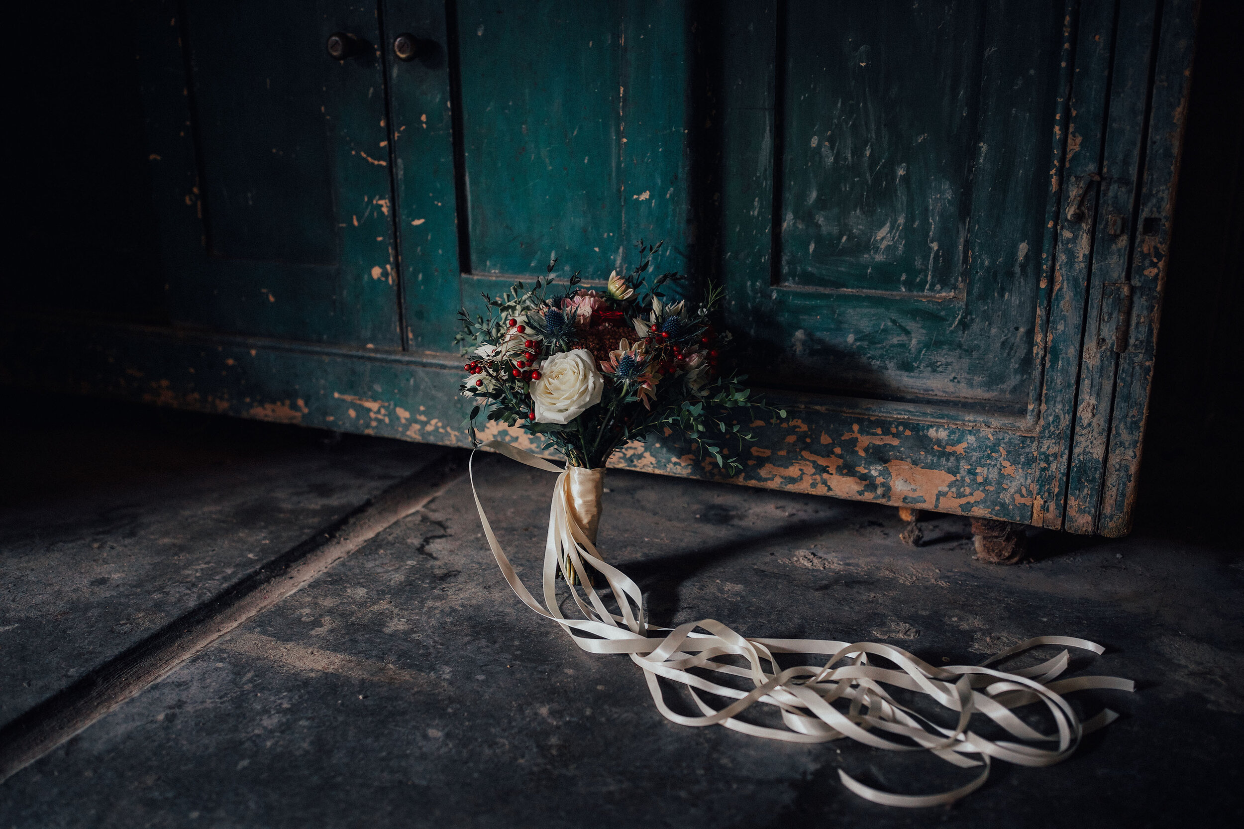 Wedding flowers tied with ribbons propped up against wooden door at Cambo estate 