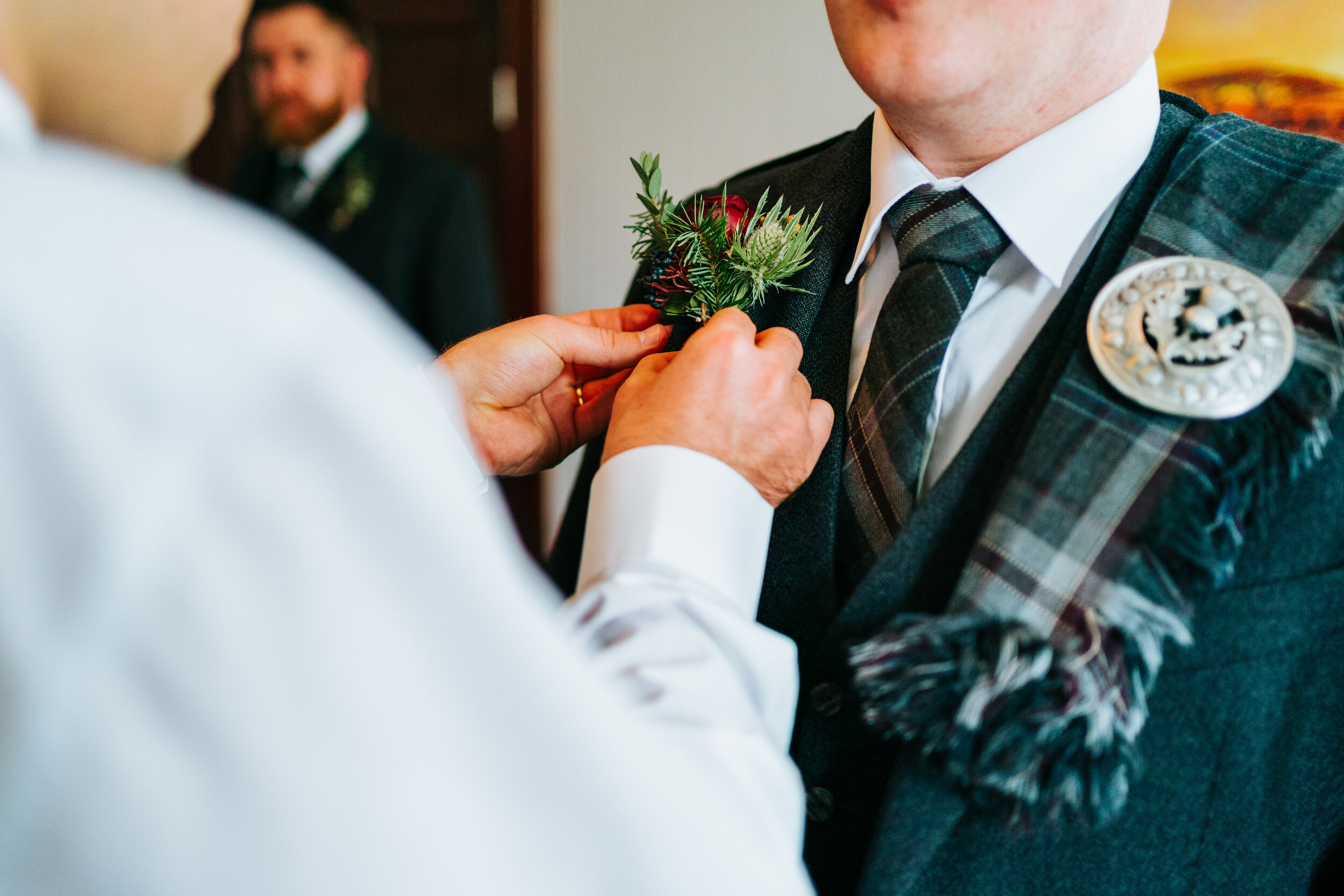 Scottish thistle button hole being attached to Groom at Cambo Estate