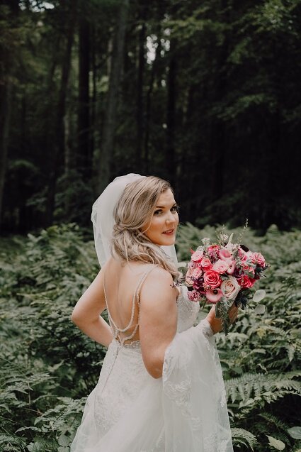 Scottish bride holding pink wedding bouquet looking back at camera at Piperdam