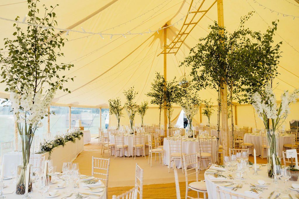 Bright and airy wedding marquee featuring white linen and green foliage