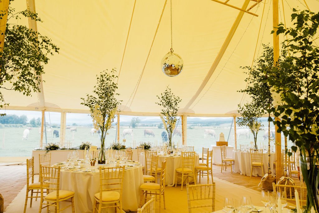 Inside of marquee at Perthshire wedding featuring tall foliage centerpieces and white interior 