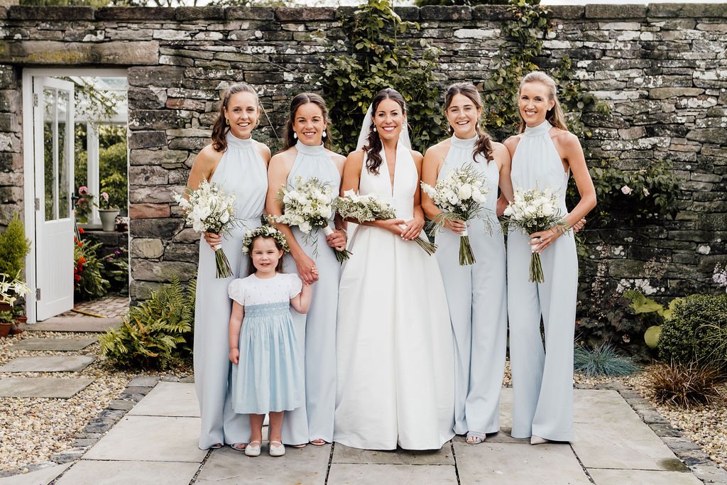 Bridal party group photo holding white bouquets and wearing light grey jumpsuits