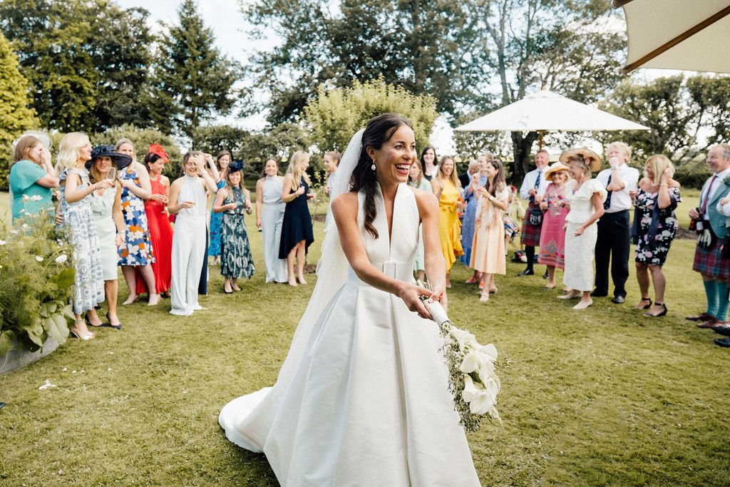 Bride about to throw her white wedding bouquet at summer rural wedding