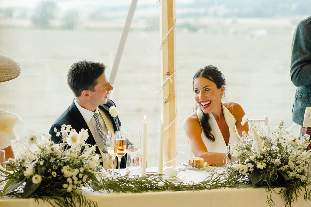 Bride and groom sharing a laugh at top table of Scottish country wedding