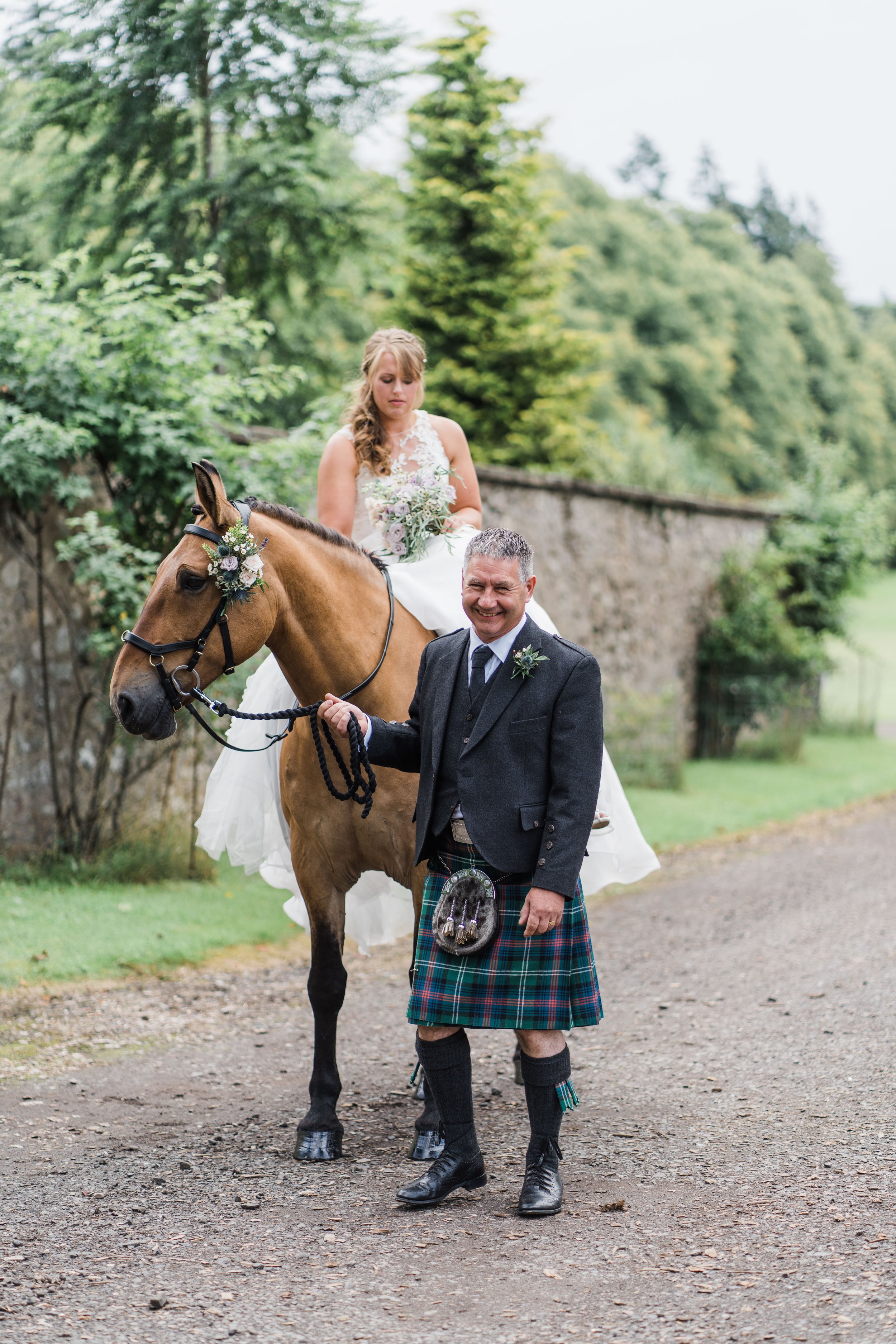 Groom standing with bride on horseback at country summer wedding 