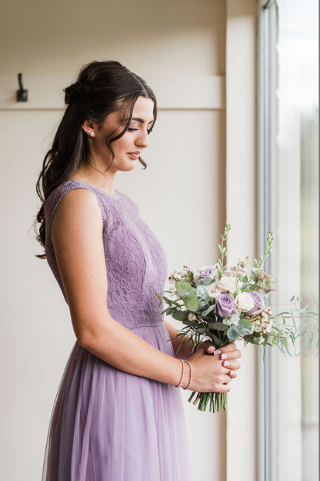 Bridesmaid standing by window holding romantic floral bouquet