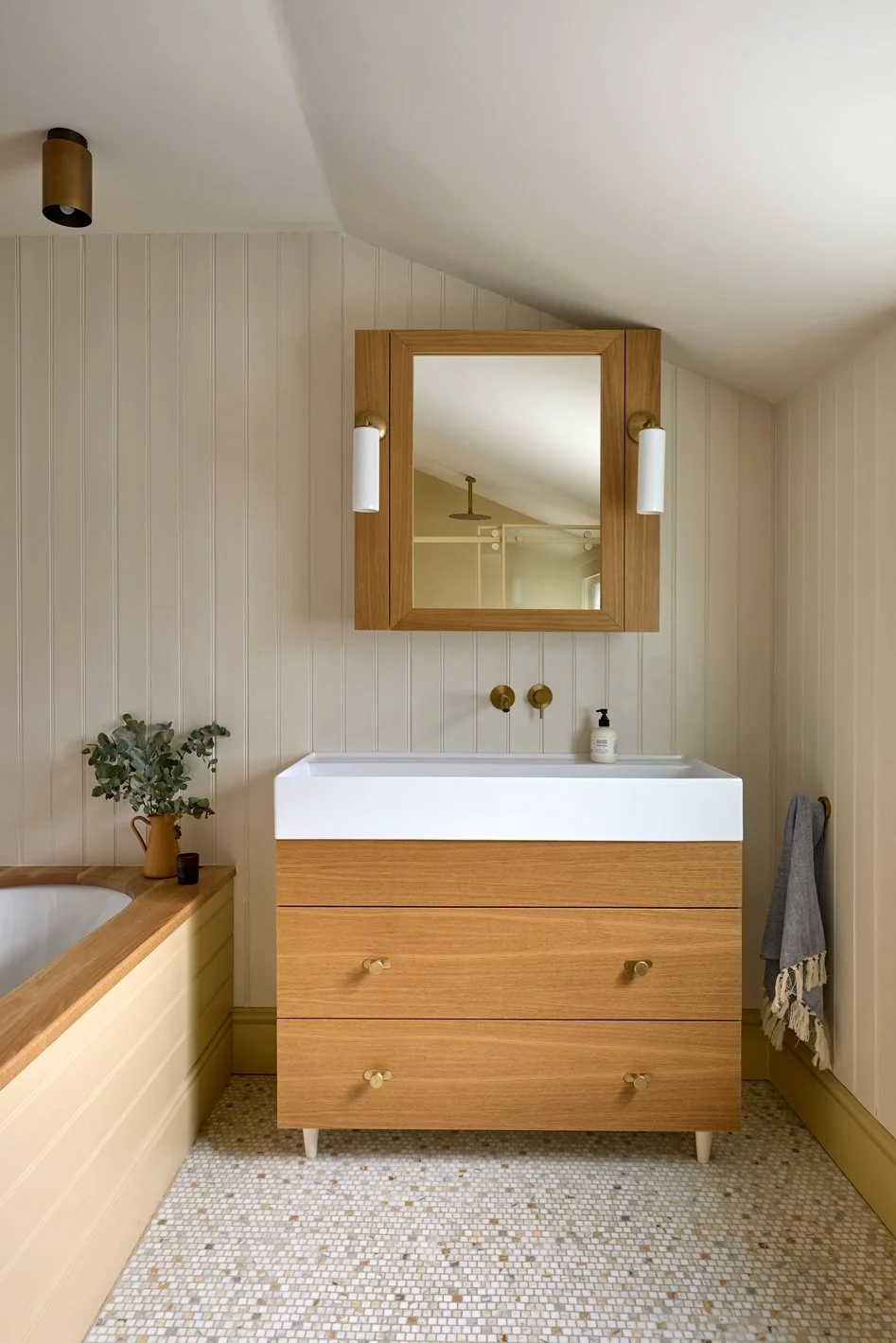  The refurbished bathroom is shaped around a soft palette of warm yellow tones, with painted cladding and tadelakt shower walls creating a sense of calm continuity throughout the space. Marble mosaic flooring introduces subtle texture and colour unde