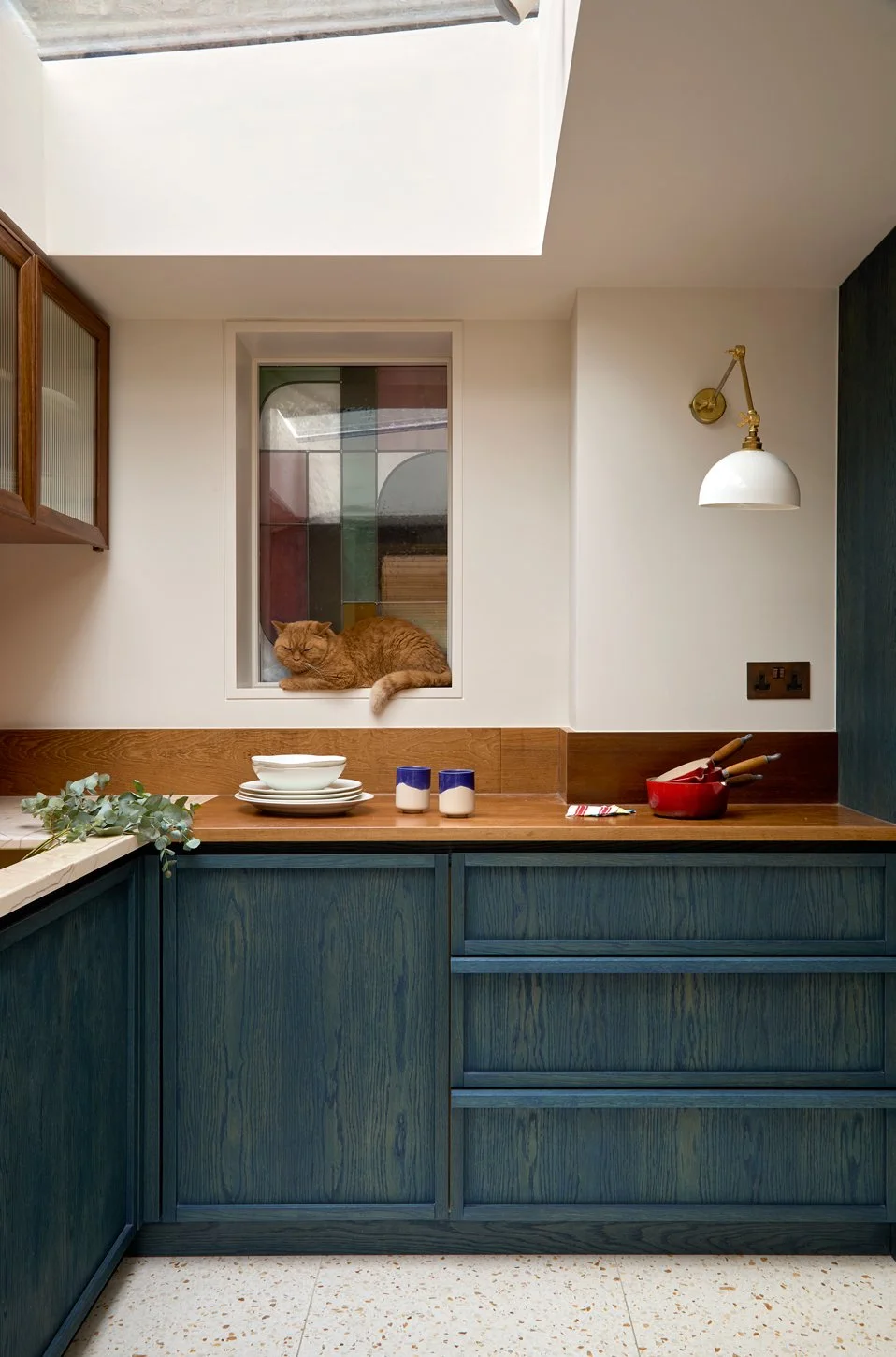  Natural light pours into the new kitchen extension through a large rooflight above, illuminating a rich palette of deep blue oak cabinetry, reclaimed iroko worktops, terrazzo flooring, and warm copper detailing. Bespoke etched glazing softly filters