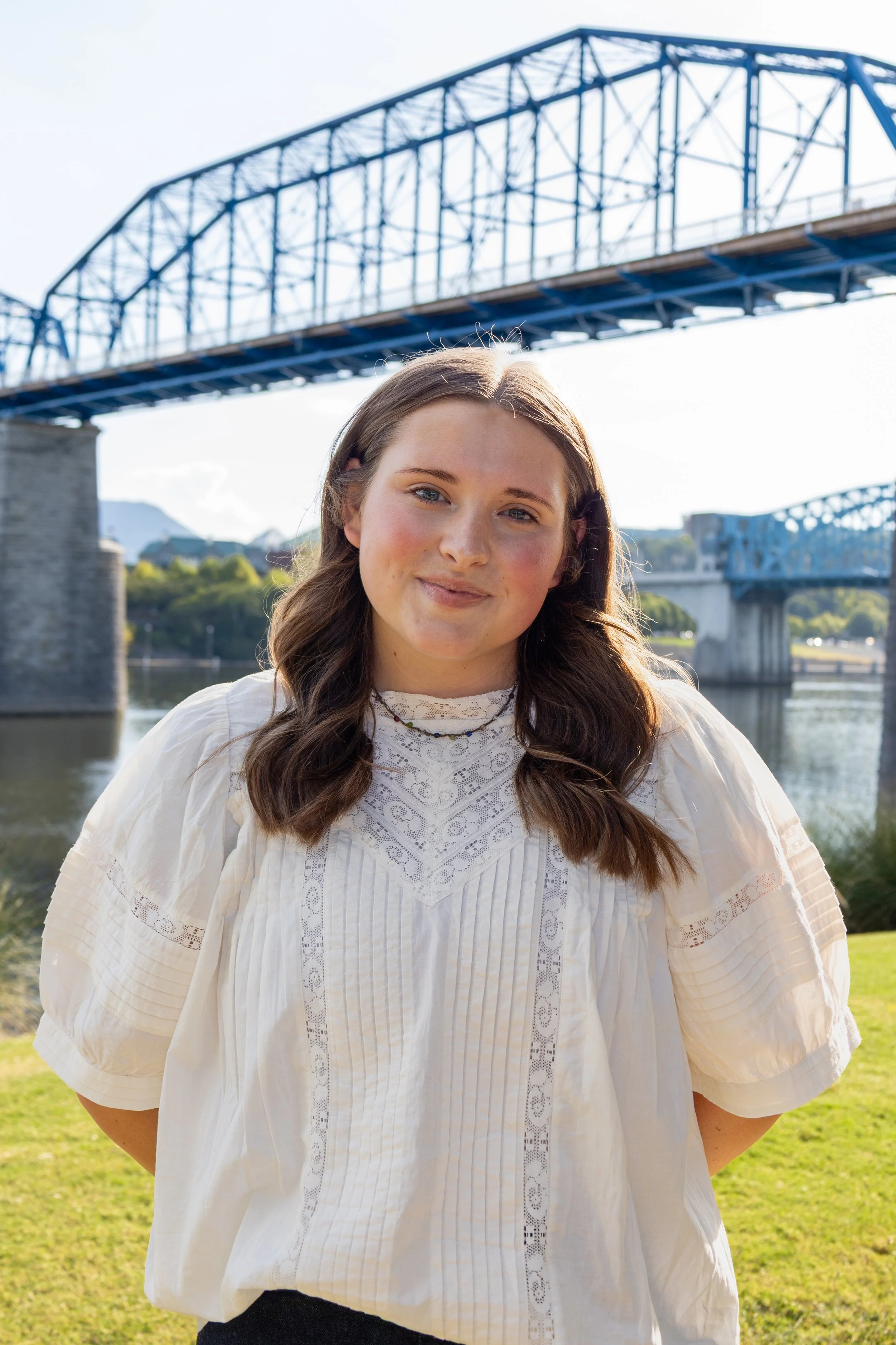 Girl standing in white shirt beneath a blue bridge in front of a river.