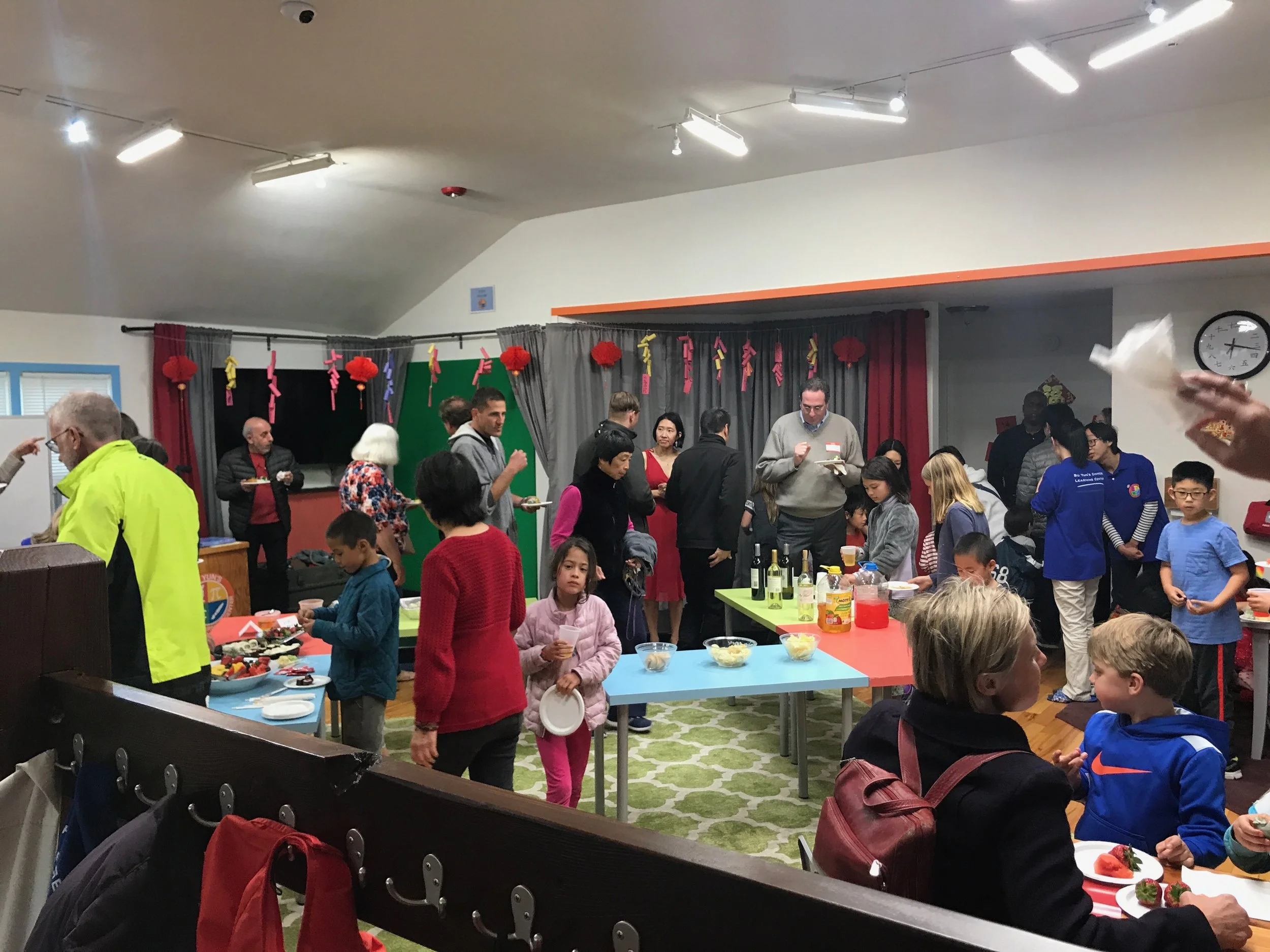 People gathered in a room decorated with red lanterns and hanging paper decorations, enjoying food and socializing at tables during a celebration or event.