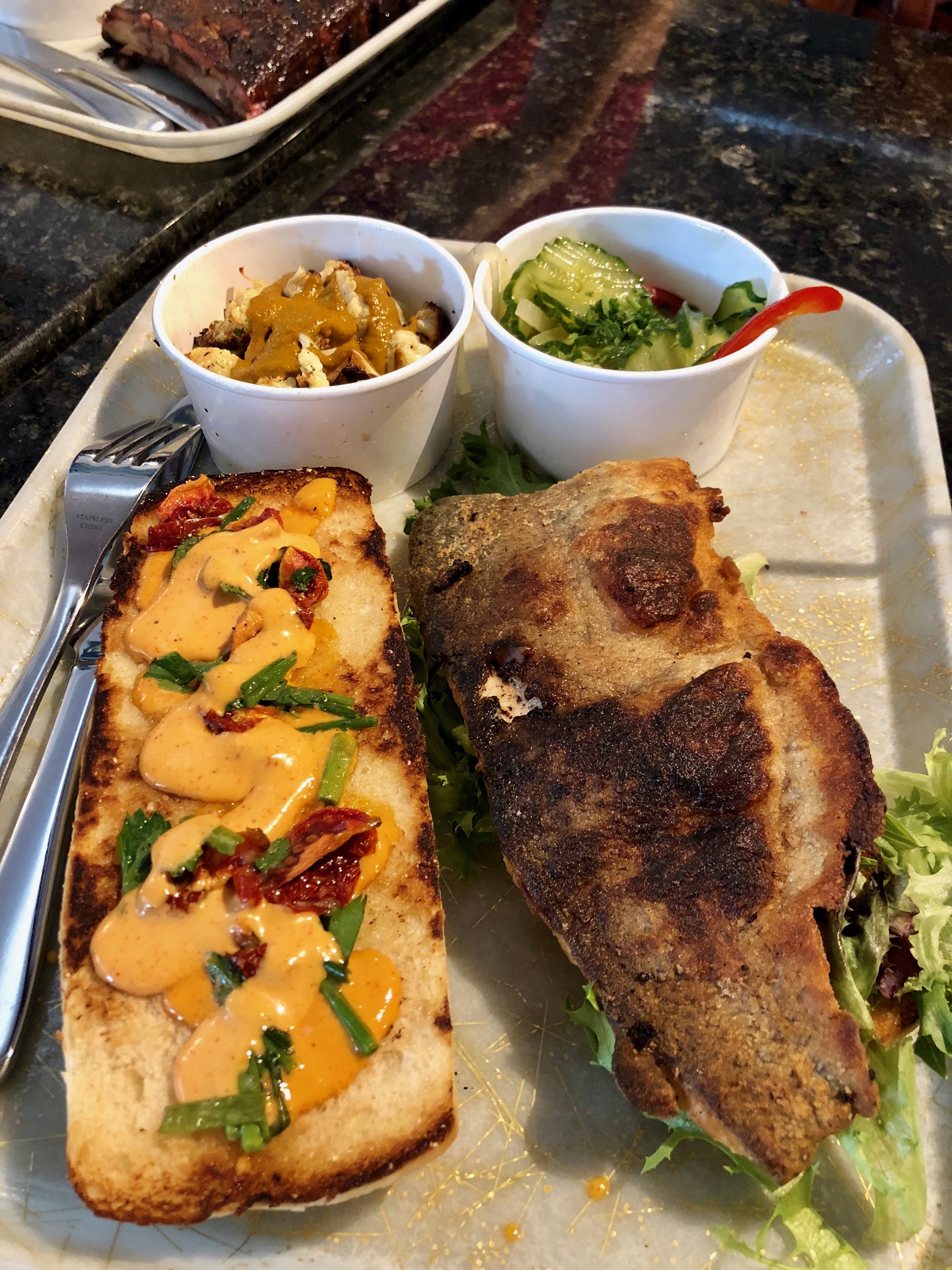 Seasonal crispy trout po’boy sandwich with seasonal sides of roasted cauliflower and cucumber salad