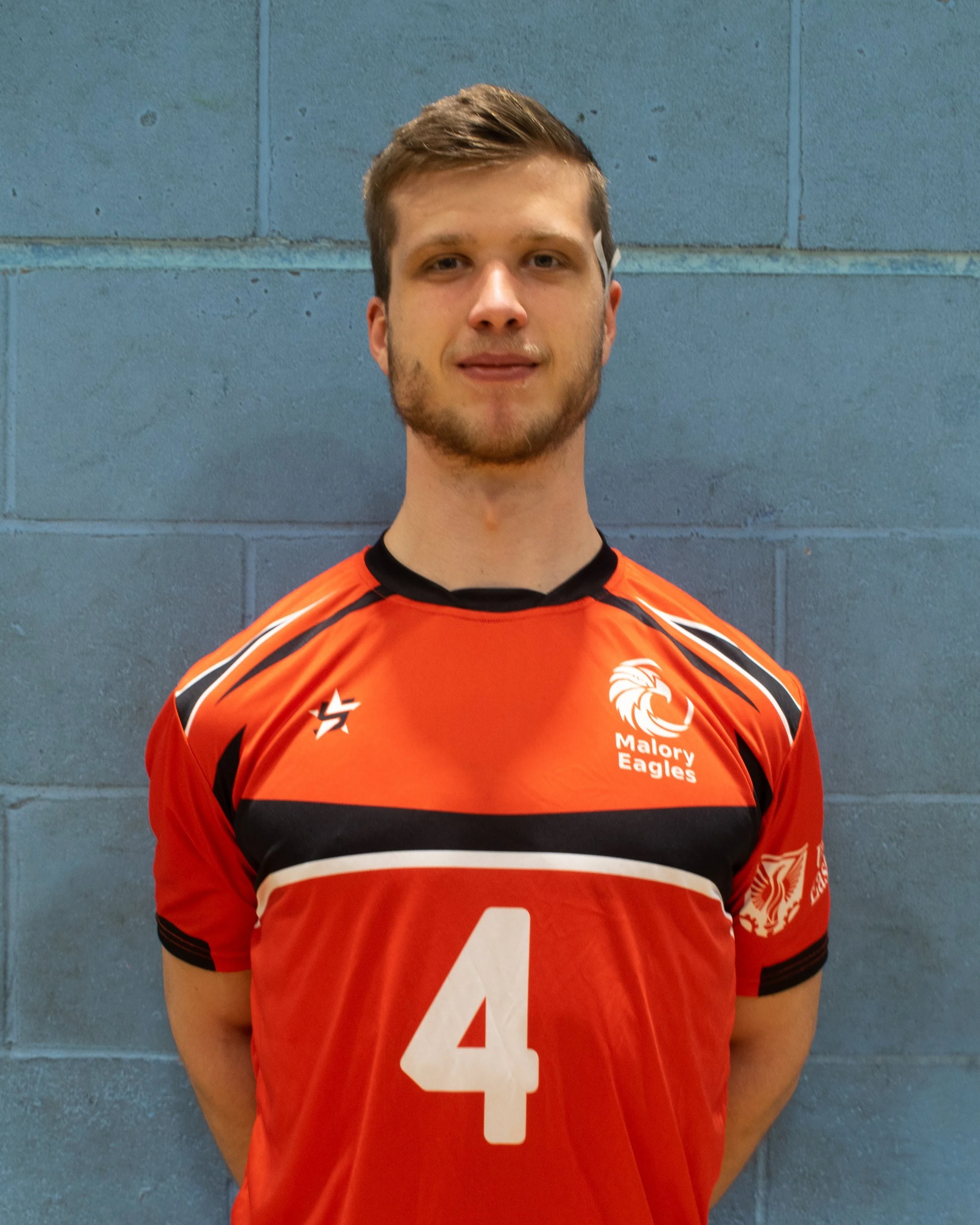 A young man in a red sports jersey with the number 4, standing against a blue cinder block wall.