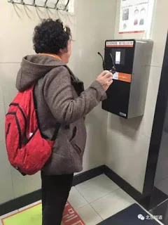 A Chinese woman standing in front a face-scanning machine to wait for her face to be scanned. The paper is only available after the scan finishes. 一名北京婦女站在「人臉識別廁紙機」前等待。機器完成「識別」她的臉之後,手紙才會出來。