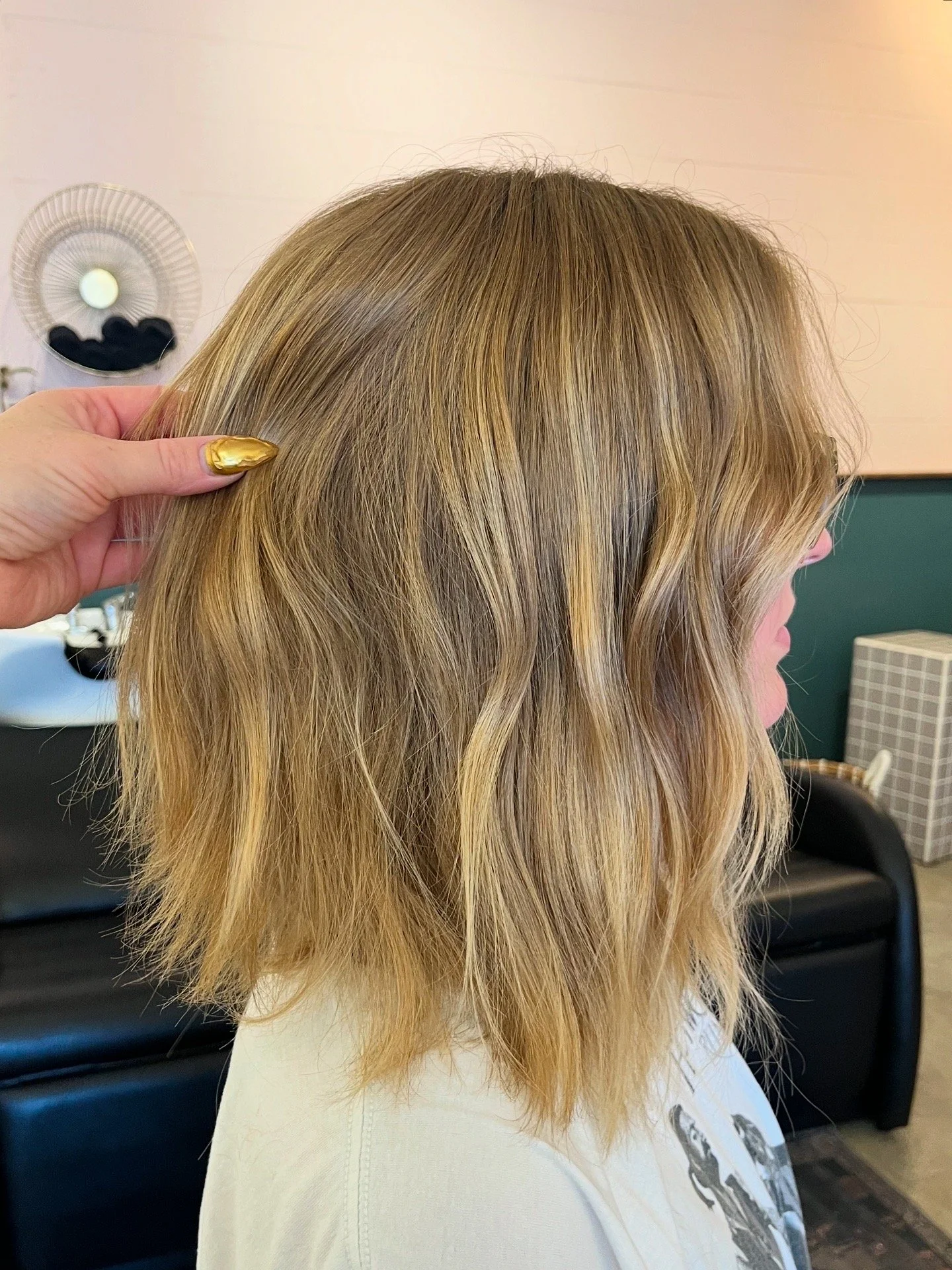 Close-up of a woman with blonde, wavy hair in a salon, with a hand touching her hair, showing the layered hairstyle.