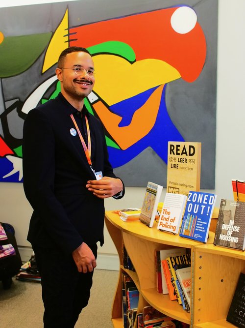 DivComm member Addison Vawters poses with the Uni Project library, featuring books by heterodox authors in social justice and urban planning