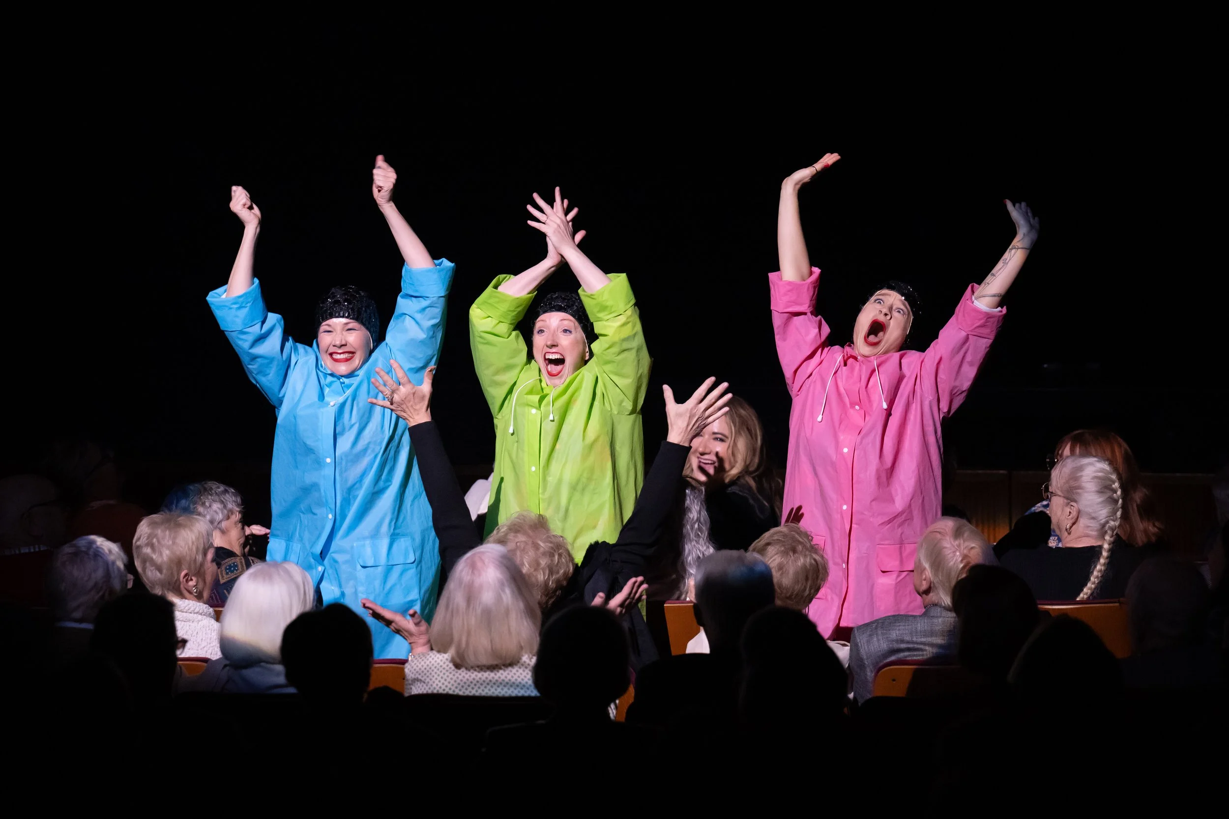 The Seaweed Sisters performing at the McCallum Theatre with arms raised, engaging the audience during a live performance.