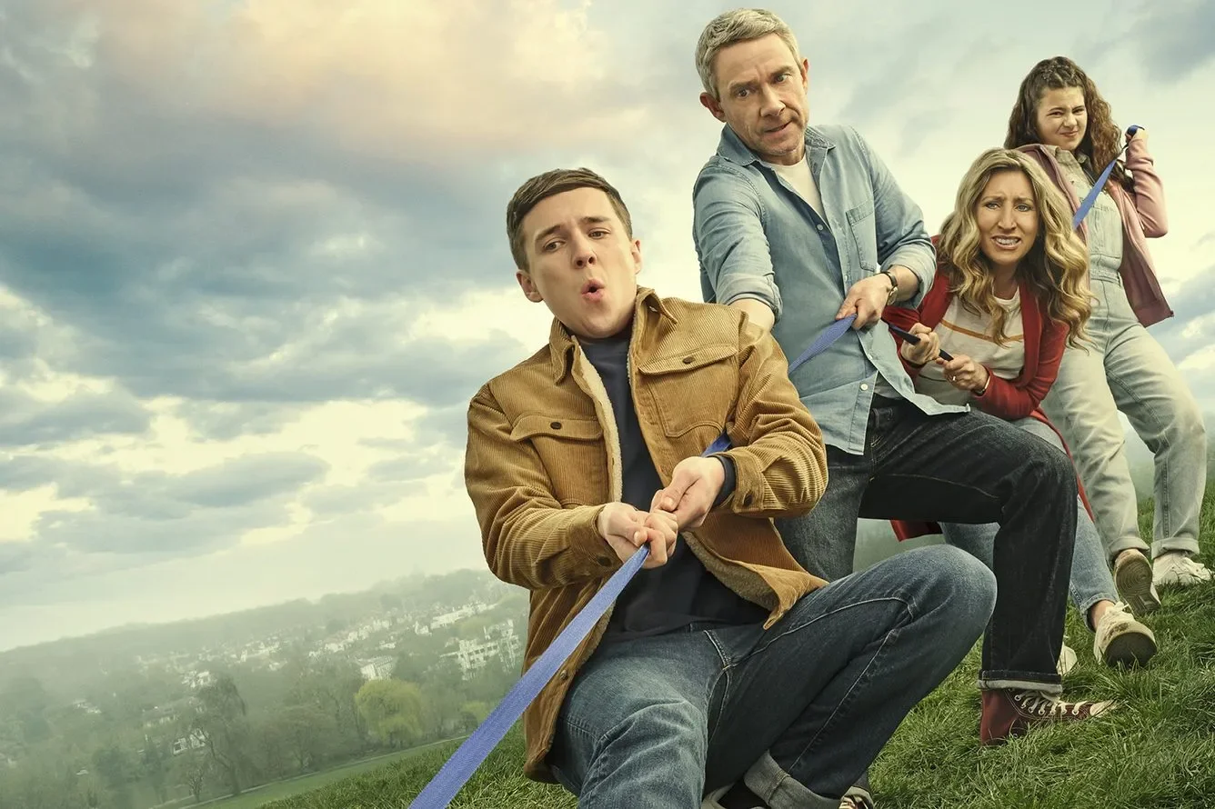 A group of five people pulling on a rope in a grassy field outdoors with cloudy sky background, expressing various emotions.