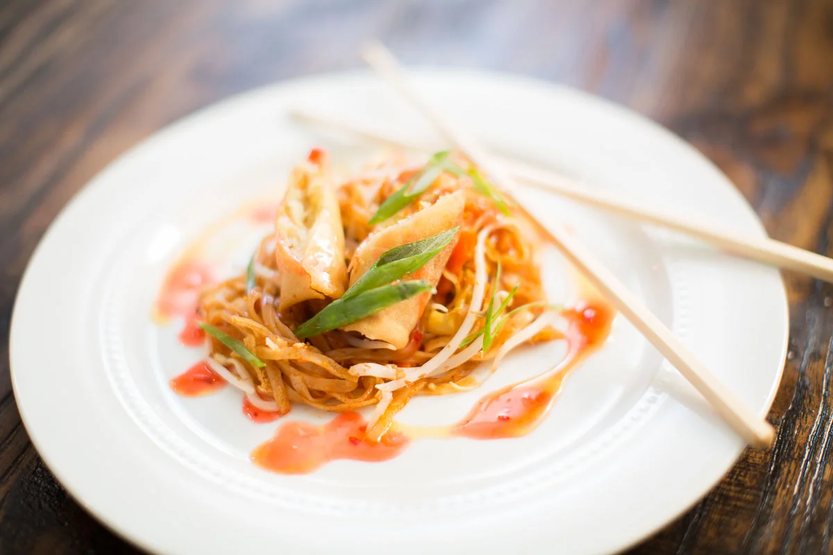 Tia Noodles & Vegetables topped with Vegetable Spring roll with chili sauce and Pomegranate glaze 
