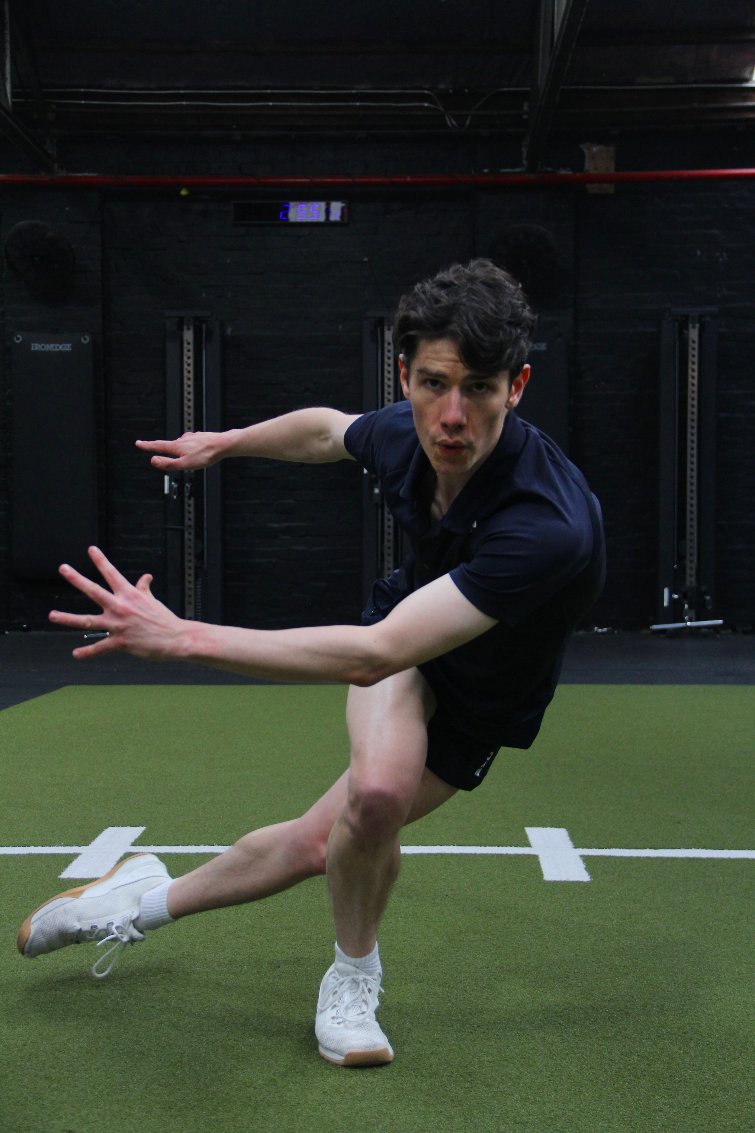 Young man in athletic clothing doing a dynamic exercise on a green turf in a gym.