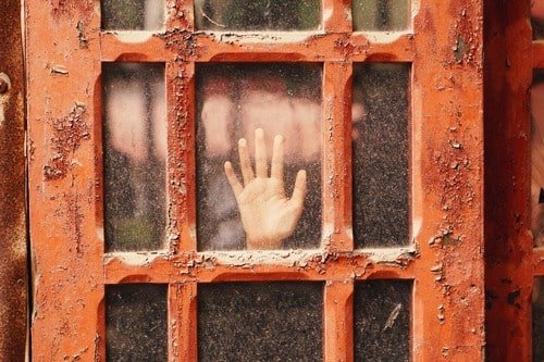 Hand against a glass door representing the ways holding on to hope can keep us trapped