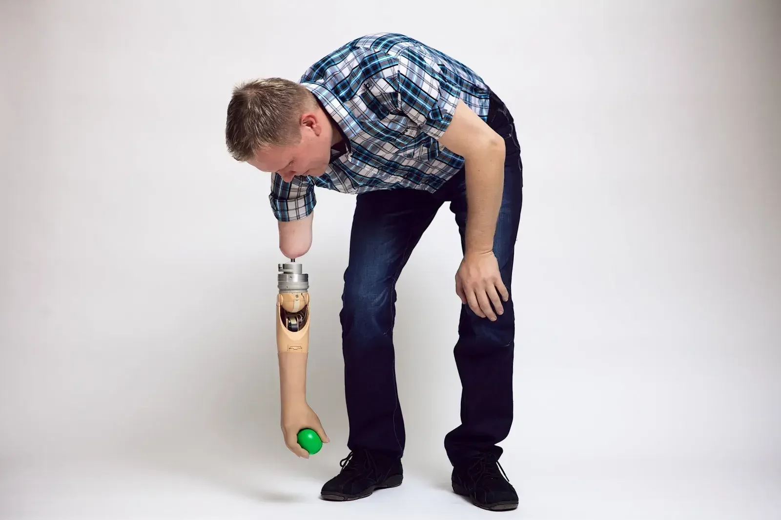 A man with a prosthetic arm bent over and holding a green ball with his prosthetic hand.