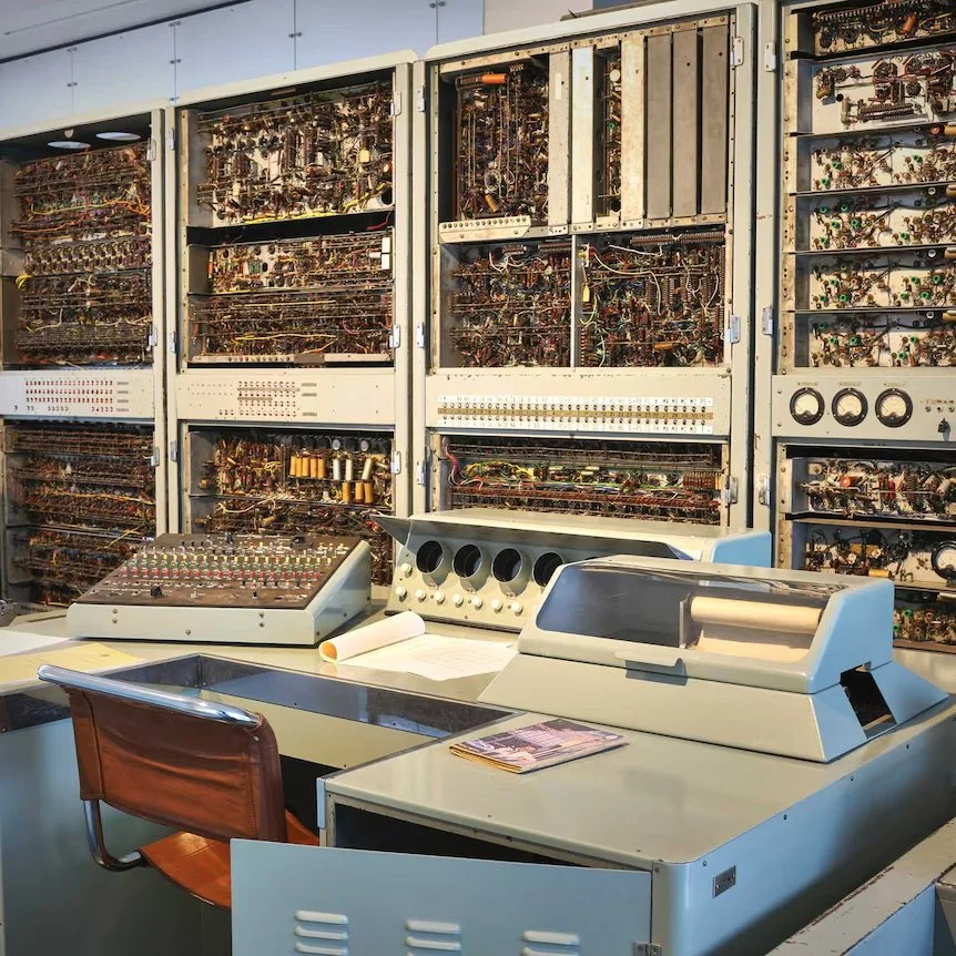 A room filled with vintage computer technology and circuit boards, including an oscilloscope, analysis equipment, and a cash register.