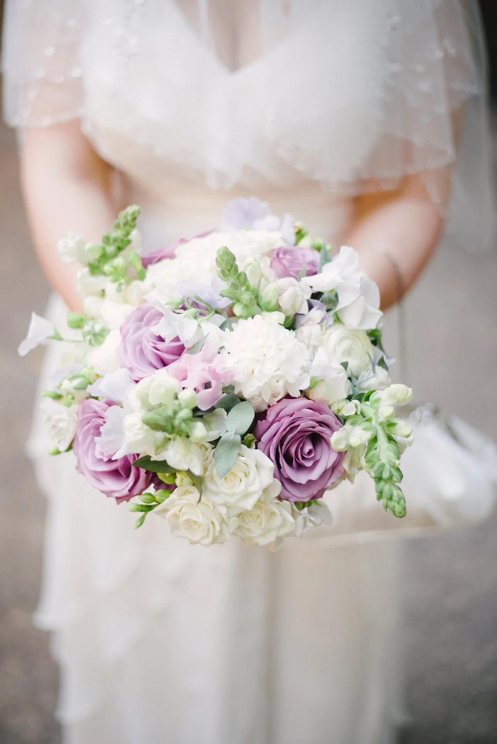 brides bouquet in white and lilac spring flowers to include roses, snapdragons and fragrant freesia