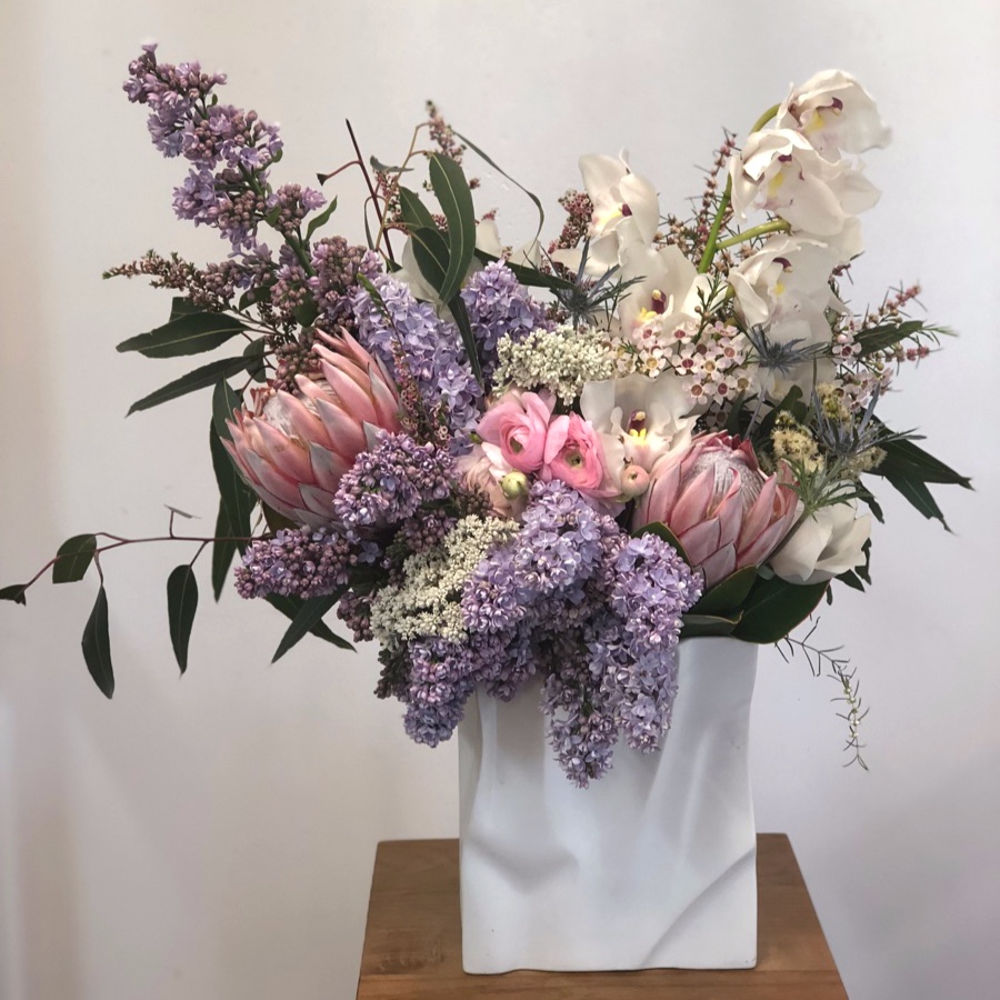 paper bag vase filled with king protea, lilac and orchids by Darwin florist Beija Flor
